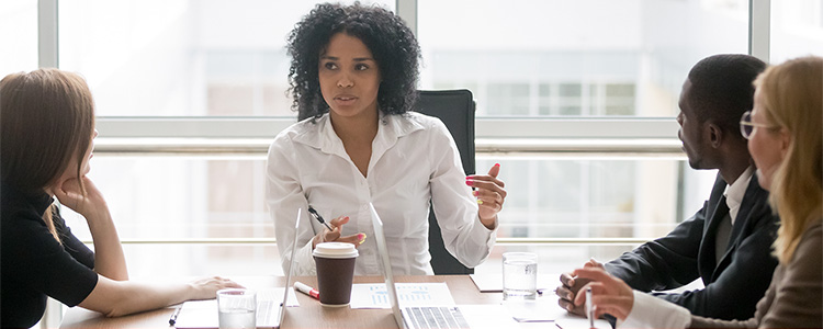 woman at conference table in front of large window talking to others at table